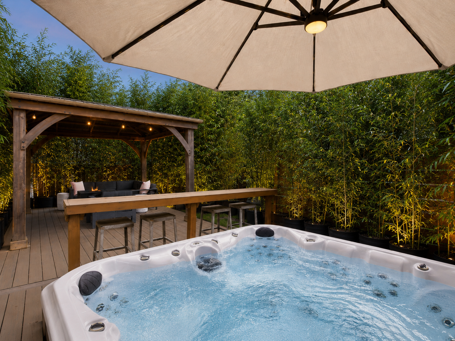 The same hot tub and deck, now wrapped in a wall of mature black bamboo with warm uplighting at the base — the neighbor's house is gone, the deck reads as a private spa surrounded by green